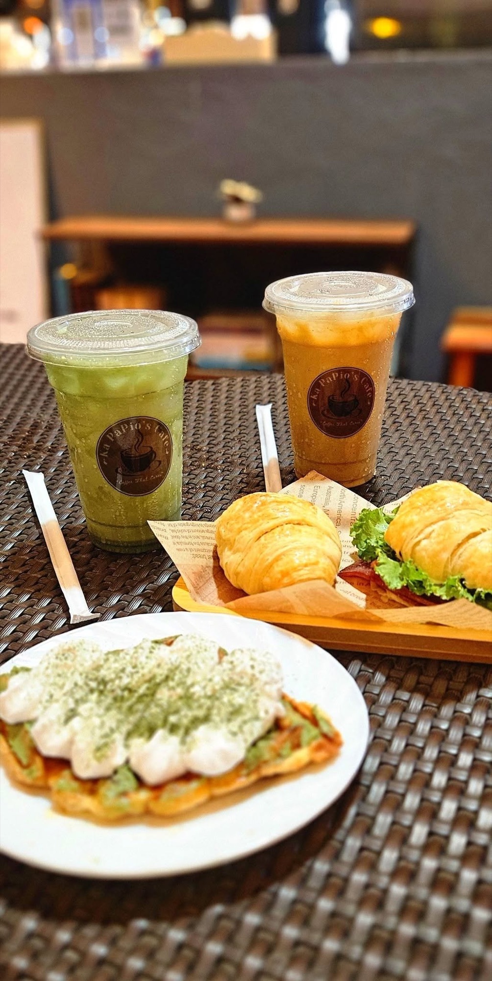 Two iced drinks with croissant sandwiches on a wooden board