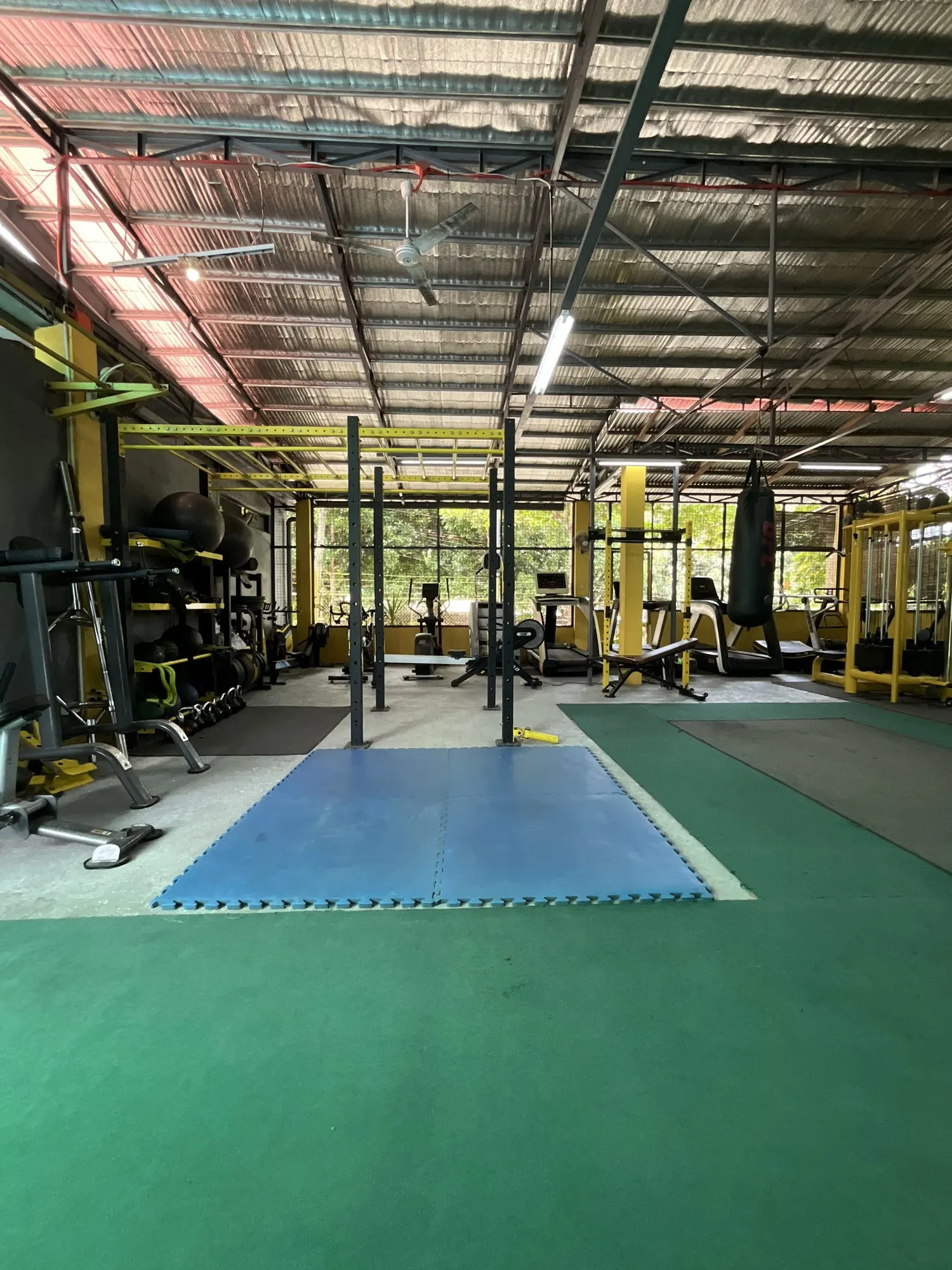 Wide view of the open-air gym floor with mats, rig and heavy bag