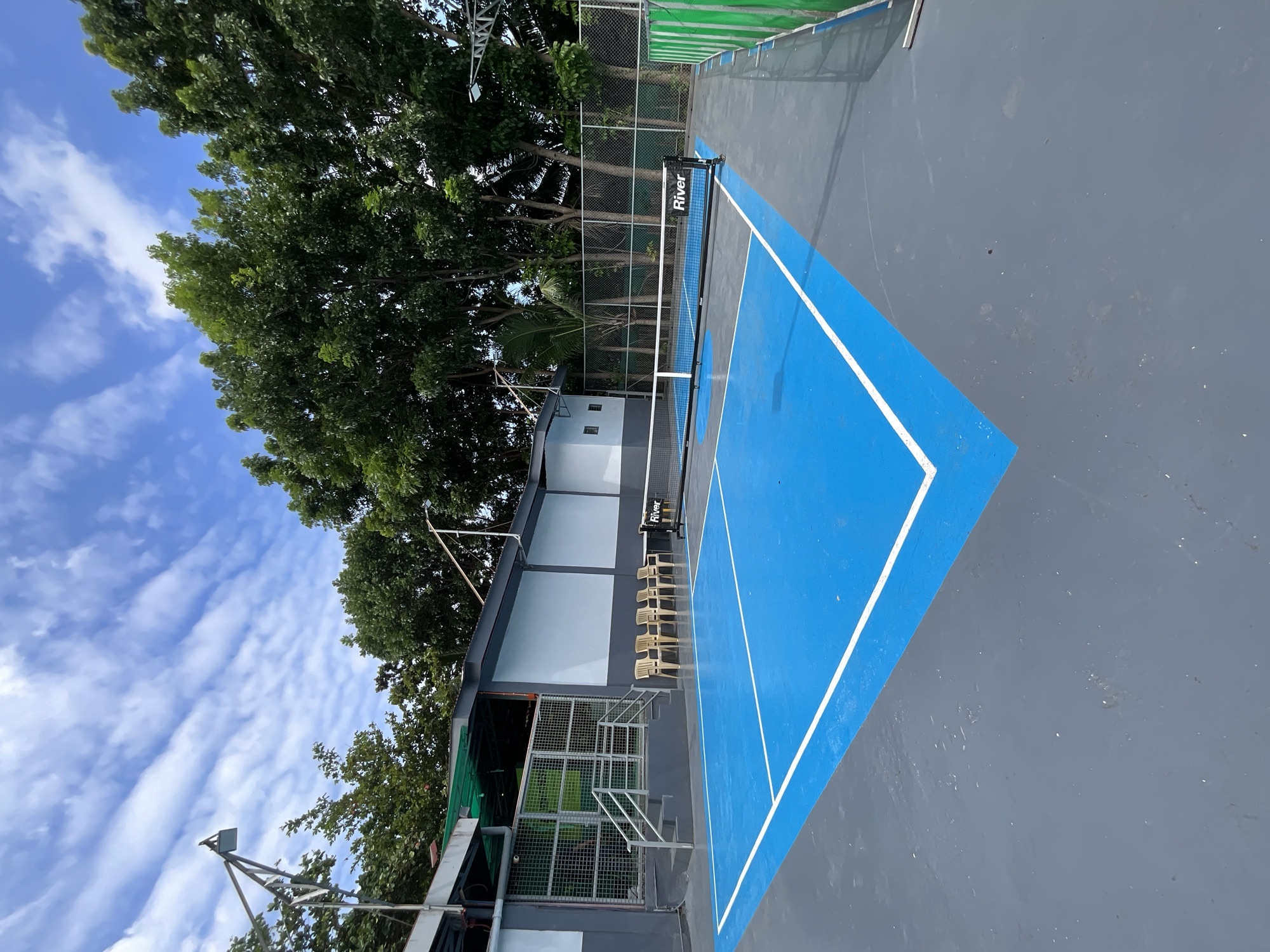 Pickleball court with the net up, seating along the fence and trees behind