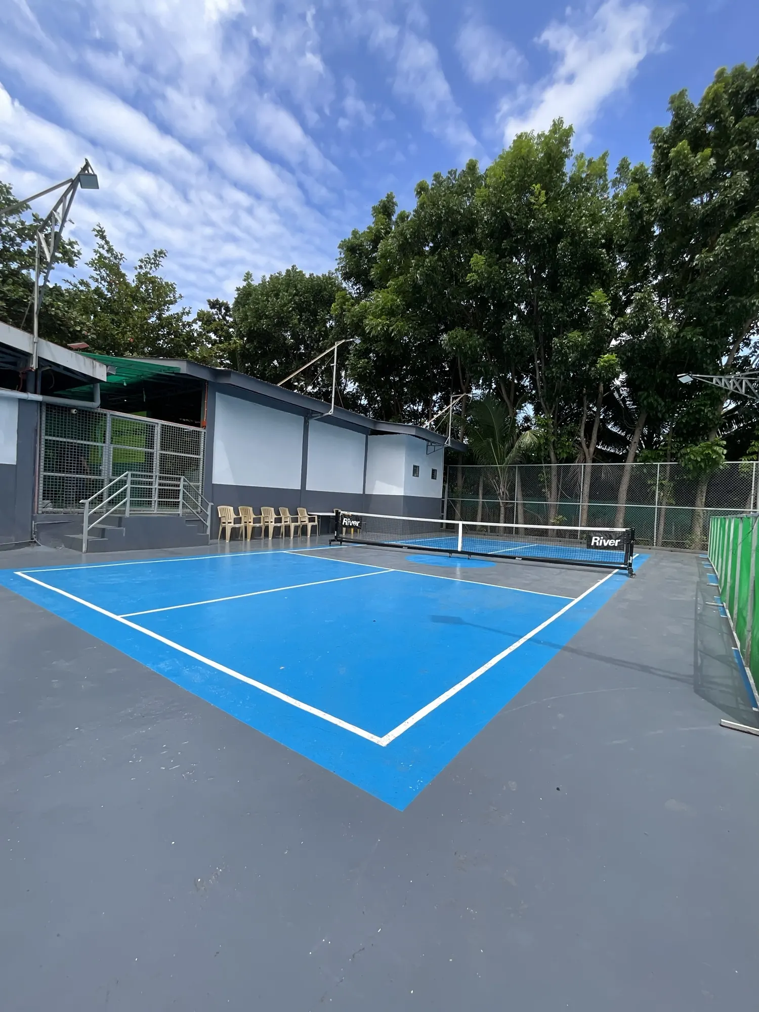 Pickleball court with the net up, seating along the fence and trees behind
