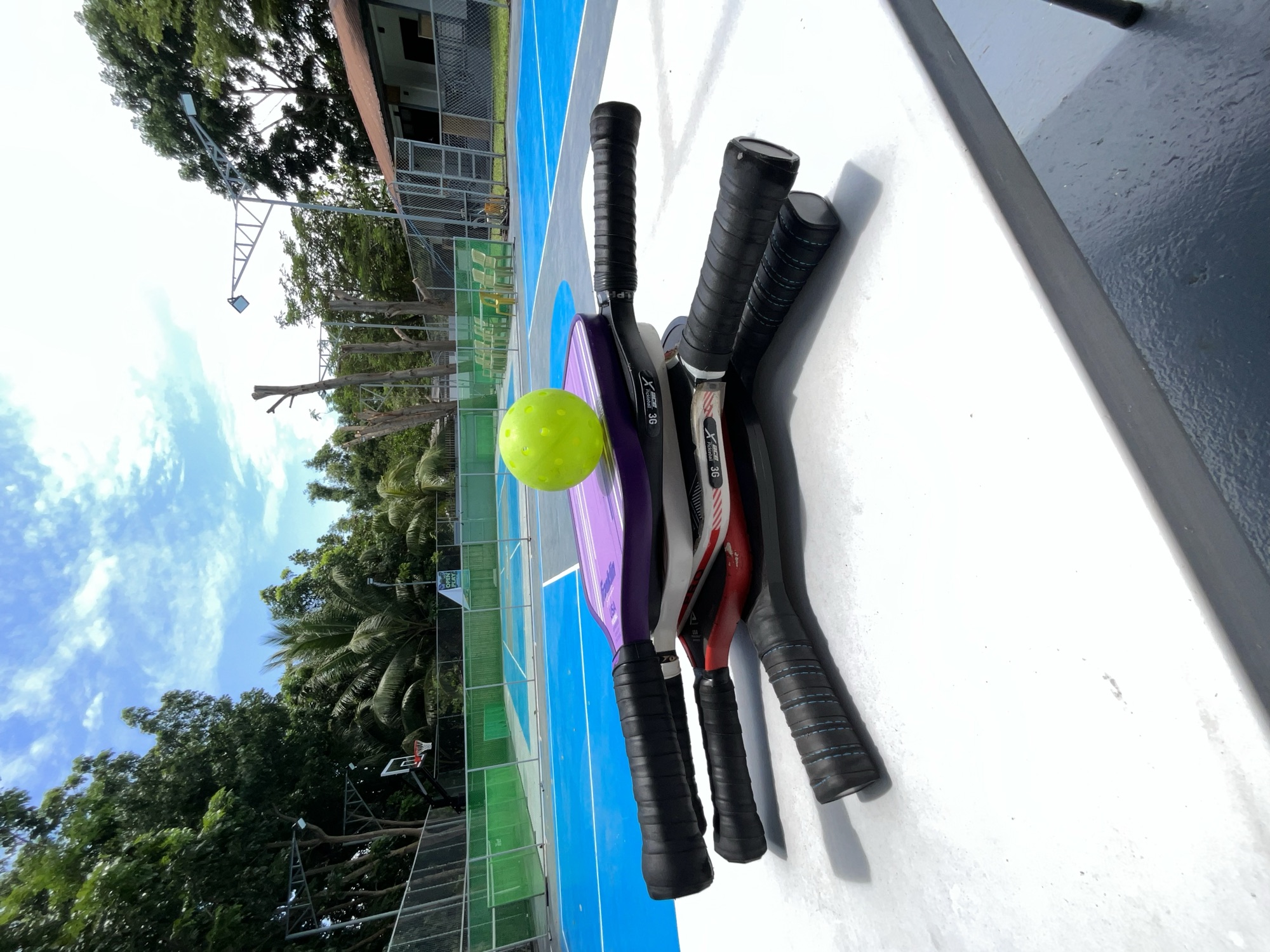 Two pickleball paddles and a yellow ball resting on the court surface