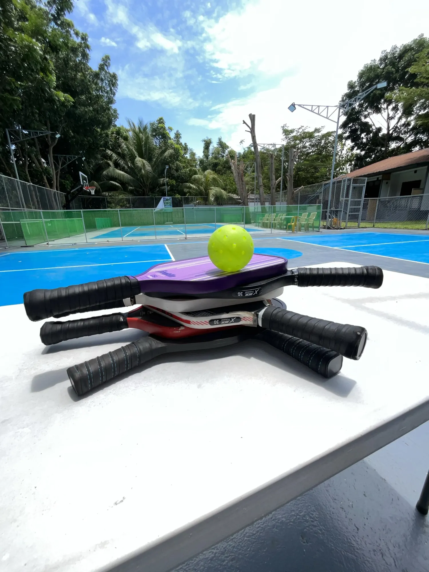 Two pickleball paddles and a yellow ball resting on the court surface